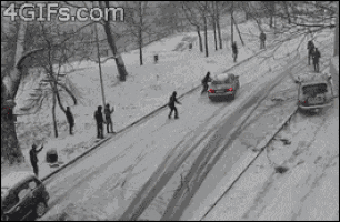 A car struggles to drive in the snow, and proceeds to slip sideways down a snow covered hill. pedestrians try to help stop the sliding car without prevail.