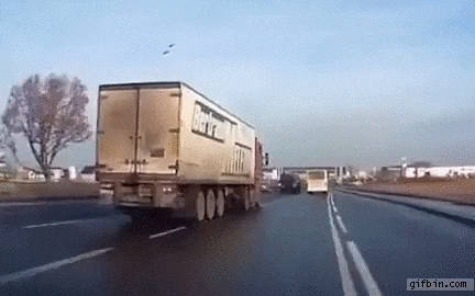 A semi truck skillfully swerves into the left lane on a freeway, narrowly avoiding stopped traffic ahead.
